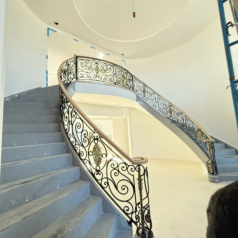 Curved staircase with a wrought scroll balustrade and wood handrail in a round stair hall