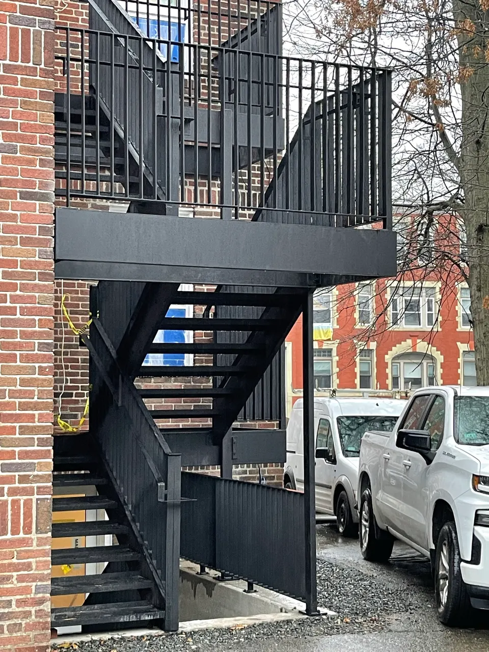 Black steel egress stair with landing and guardrails beside a brick building