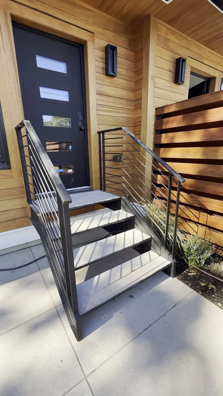 Black steel entry stair with horizontal-bar railings at a wood-clad front door