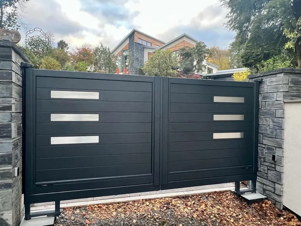 Dark double driveway gate with horizontal panels and metal inserts between stone-faced piers