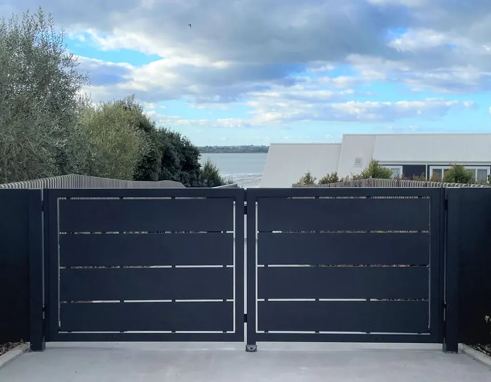 Black double gate with horizontal bands in a solid fence line with water in the distance