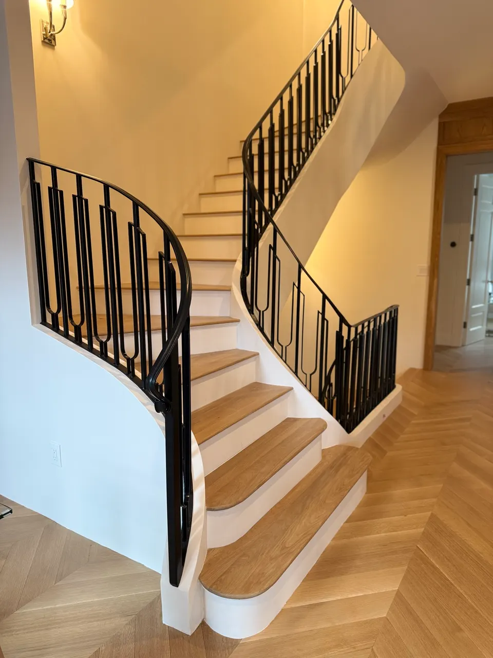 Black railing with curved end following a white staircase with wood treads