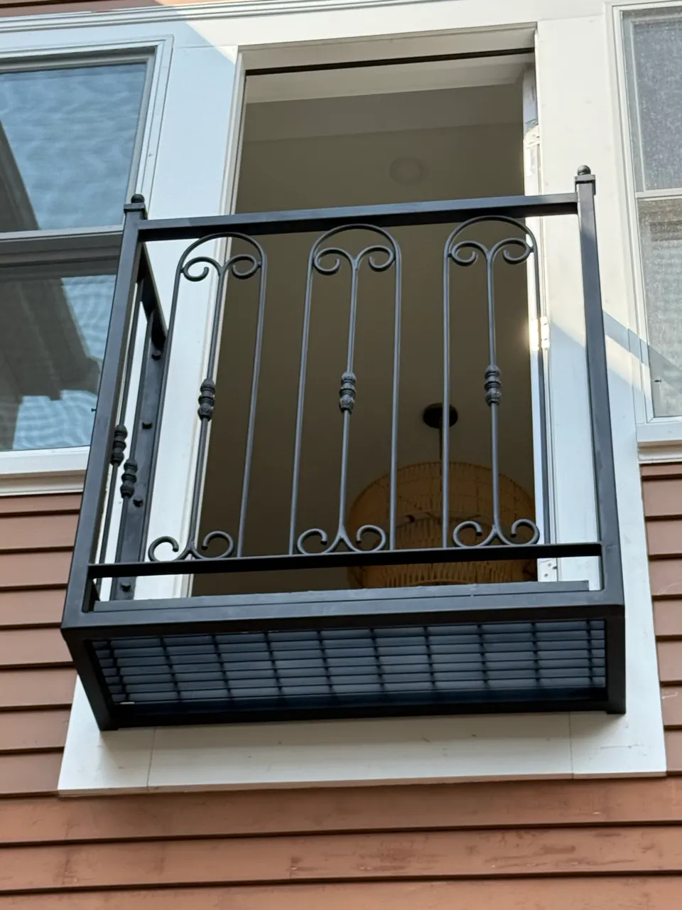 Black Juliet balcony with scroll details and a steel base on a wood-sided house