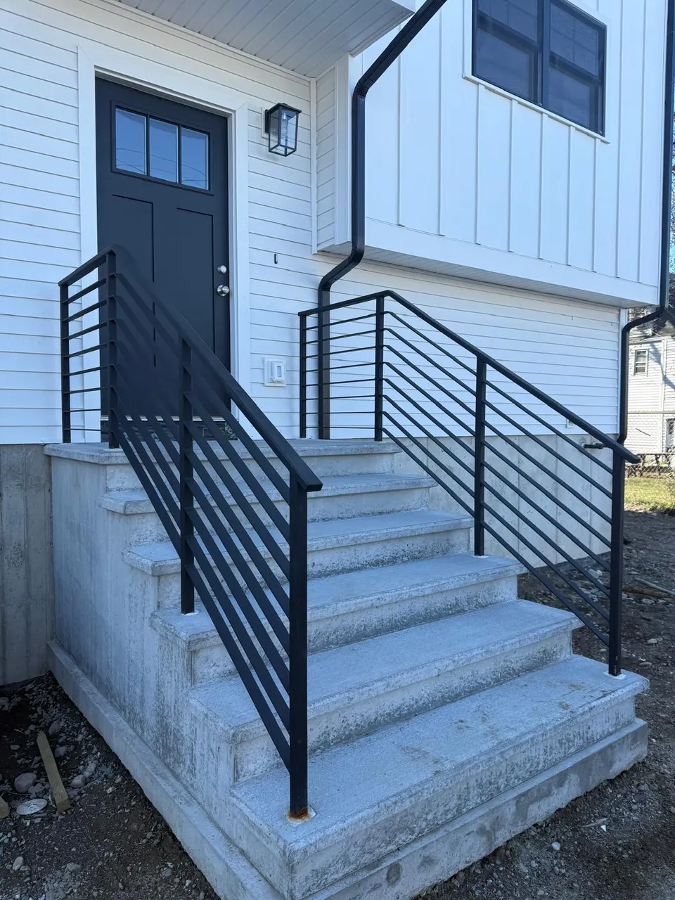 Black horizontal-bar handrails on concrete entry steps at a front door