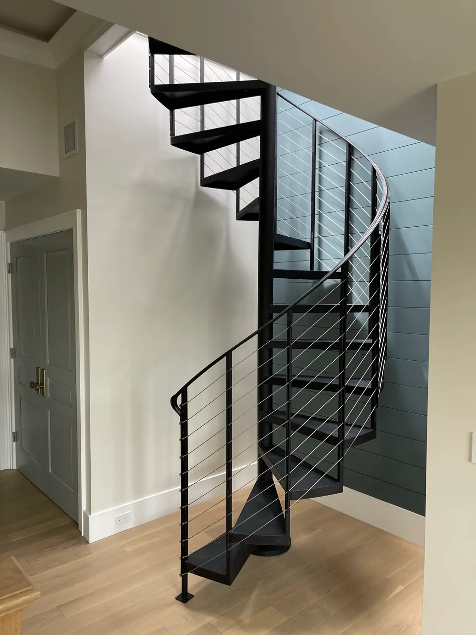 Black interior spiral stair with cable railing beside a teal wall
