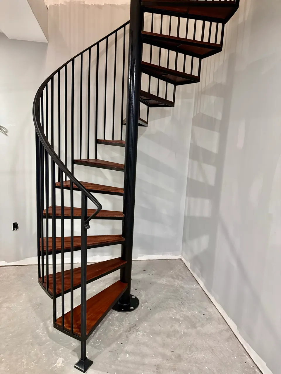 Black steel spiral stair with warm wood treads and vertical balusters
