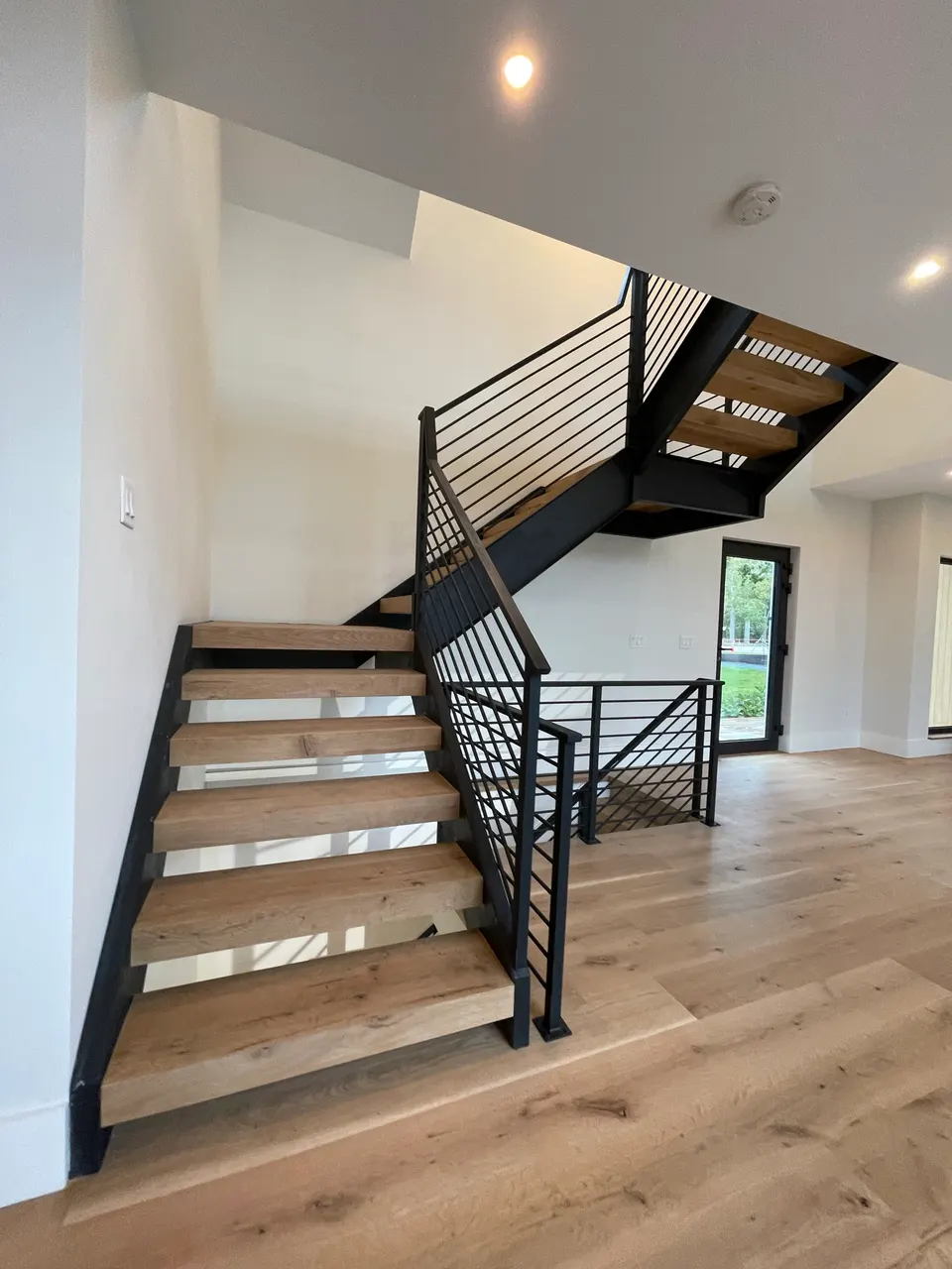 Black steel stair with wood treads and horizontal railing in a bright open room